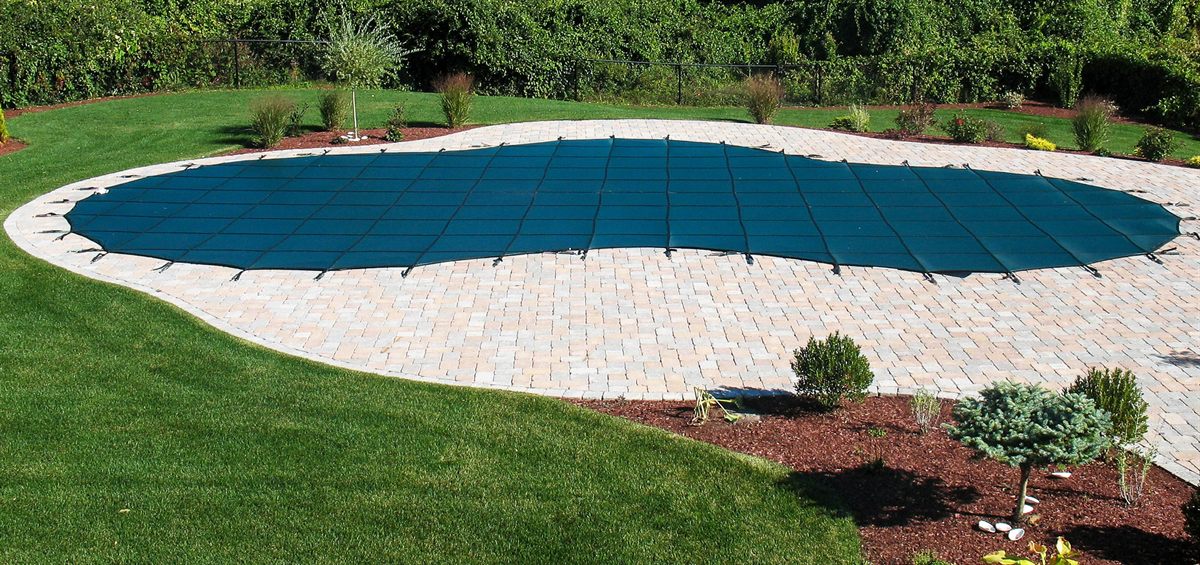 A blue Merlin mesh safety cover strapped across a closed in-ground pool on a paver patio